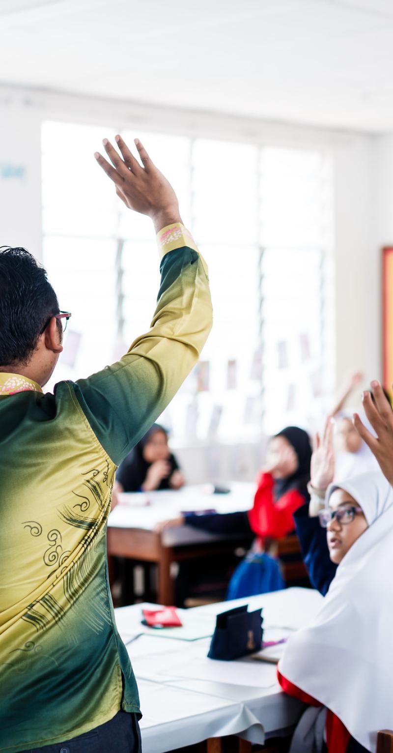 teacher asking students a question with raised hands